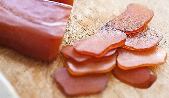 Sulla sinistra pezzo di bottarga di tonno, sulla destra fette di bottarga; il colore è quello tipico del tonno crudo, rosa quasi rosso; sotto piano in legno