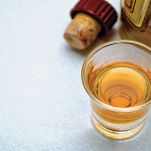 Bicchierino con liquore, con bottiglia e tappo di sughero sullo sfondo