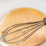 three beaten eggs for cooking French omelet in a glass bowl before whipping. Whisk for whipping lies in a bowl.