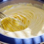 Closeup of electric mixer with whipped smooth dough for cake. Batter being whipped. Mixing white dough in bowl with motor mixer,