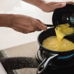 Donna versa uova sbattute in padella per fare omelette