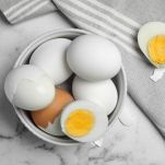 Hard boiled eggs and kitchen towel on white marble table, flat lay