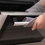 Woman putting baking tray into electric oven, closeup