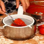 Donna filtra il succo dei pomodori con un colino