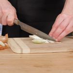 Donna taglia cipolle gialle su un tagliere di legno