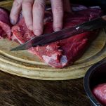 Mani tagliano carne di manzo cruda su tagliere di legno