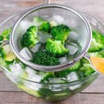 Blanched broccoli cabbage florets in a sieve in icy water on wooden table