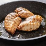 Pan-fried juicy chicken breasts on a dark pan.
