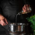 The chef adds oil to saucepan while making dumplings. Working environment on vintage kitchen table in restaurant. Vertical image