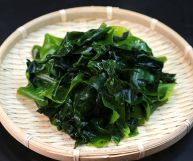 Su un piatto rotondo di bambù tipico della cucina giappinese, alghe wakame saltate in padella pront per essere mangiate; sfondo nero