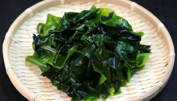 Su un piatto rotondo di bambù tipico della cucina giappinese, alghe wakame saltate in padella pront per essere mangiate; sfondo nero
