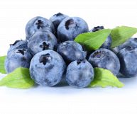 Mirtilli neri con foglie verdi, isolati su uno sfondo bianco; l’aspetto è carnoso e invitante, il colore varia dall’azzurro al viola e la superficie opaca