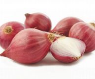 Su sfondo bianco scalogni freschi interi, con buccia rossa tendente al bordeaux, pronti per essere cucinati; una metà presenta falde bianche