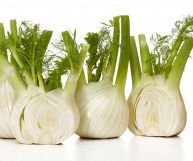 Su uno sfondo bianco, due finocchi interi e due tagliati a metà; perfetti per le insalate perché hanno una forma tondeggiante, gambi e foglie verdi