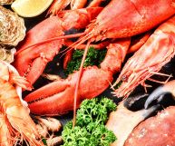 Da sinistra a destra: ostriche, gamberoni, aragoste e gamberi freschi, tutti con gusci e carapaci, con alcune fettine di limone e ciuffetti di prezzemolo