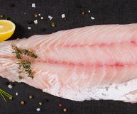 Su fondo scuro, un filetto di pesce persico pronto per essere cucinato; le carni sono rosa chiaro, con margini bianchi e due strisce tendenti al fucsia