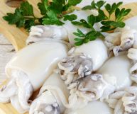 Seppie intere con i loro tentacoli, pulite e pronte per essere cucinate; la pelle e lucida e chiara; sono posate su un tagliere di legno con prezzemolo