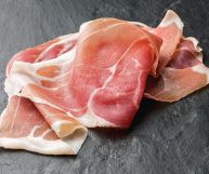Culatello a fette su fondo in ardesia: il colore è rosato, con sfumature più intense e striature bianche della parte più grassa