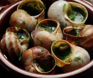 Chiocciole dal guscio marrone striato di bianco, arricchite da prezzemolo tritato e impiattate in un coccio rotondo; una squisitezza tutta da gustare