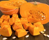 Una zucca mantovana tagliata a metà e alcuni pezzi più piccoli; la polpa è arancione intenso, consistente e dolciastra, pronta per essere cucinata