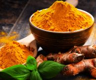 Radici di curcuma fresca arancione brillante, ciuffo di basilico verde e una scodella di legno riempita con curry color senape