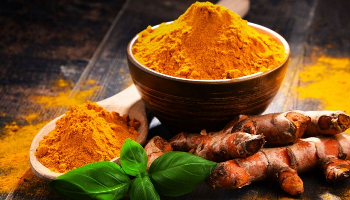 Radici di curcuma fresca arancione brillante, ciuffo di basilico verde e una scodella di legno riempita con curry color senape