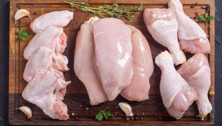 Da sx a dx, quattro ali di pollo, tre petti e quattro cosce di pollo pronte per essere cucinate; erbe aromatiche e aglio; il tutto su un tagliere