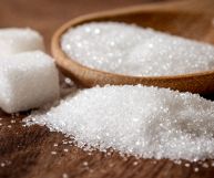 Zollette e zucchero bianco raffinato, dai granelli regolari, in parte rovesciato su un tavolo in legno, in parte contenuto in una scodella bassa di legno