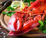 Un'aragosta con chele, antenne e carapace, pronta per essere mangiata; è condita con fette di limone e ciuffi di prezzemolo
