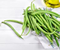 Su uno sfondo bianco, fagiolini freschi dal colore verde brillante, con le punte; in alto a destra una bottiglietta d'olio d'oliva.