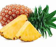 Su sfondo bianco, due fette di ananas mature con scorza; dietro un frutto intero dalla buccia aranciata, con foglie verdi brillante