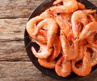 Mazzancolle fresche ancora da pulire, con il loro carapace dal colore rosa-arancione, in una ciotolo rotonda di ceramica nera: Sfondo in legno