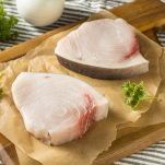 Vista dall’alto di due tranci di pesce spada pronti per essere cucinati, con la pelle attaccata e carne fresca; sono adagiati su carta posata su un tagliere