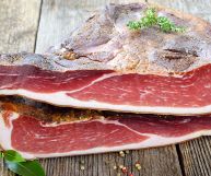 Due metà di speck su un piano rustico di legno; l'interno è rosso con parti più scure e porzioni equilibrate di grasso; l'esterno e bruno, senape e marrone