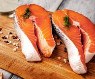 Due tranci di salmone pronti per essere cotti, con la pelle e la spina dorsale, decorati con pepe bianco in grani; le carni sono sode, di un bel colore rosato