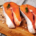 Due tranci di salmone pronti per essere cotti, con la pelle e la spina dorsale, decorati con pepe bianco in grani; le carni sono sode, di un bel colore rosato