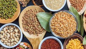 Cereali e legumi secchi come lenticchie marroni, fagioli dell'occhio, piselli, granturco, farro... Sono contenuti in scodelle bianche e cucchiai di legno