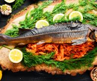 Uno storione intero pronto per essere mangiato; Accompagnano gamberetti rosa, limone a fette e erbe aromatiche verdi; piatto da portata in legno