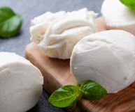 Due mozzarelle, tagliate a metà, un pezzo e una intera, con alcune foglie di basilico verde; colore bianco latte, consistenza elastica e superficie liscia