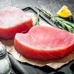 Due tranci di tonno rosso spessi 2 cm, pronti per essere cotti e insaporiti con sale, limone e rosmarino, condimenti posati sul tavolo nero