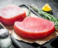 Due tranci di tonno rosso spessi 2 cm, pronti per essere cotti e insaporiti con sale, limone e rosmarino, condimenti posati sul tavolo nero