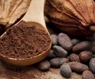 Composizione con fave di cacao marroni scuro, cacao amaro in polvere in cucchiaio di legno e guscio contenente i semi opi usati nella preparazione del cioccolato