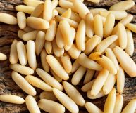 Vista dall'alto di un tavolo di legno marrone su cui è posato un mucchietto di pinoli di colore giallo pallido, probabilmente tostati