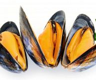 Tre cozze in posizione verticale su sfondo bianco; i gusci, neri e lucenti, sono aperti; i molluschi contenuti all’interno sono sodi, consistenti e di un bell’arancione