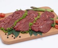 Tre bistecche di cavallo ancora da cuocere, dal colore rosso scuro dovuto alla maggiore ossidazione rispetto alla carne di vitello; su tagliere e sfondo bianco