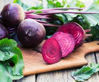 Su tagliere rettangolare, barbabietole, a fette e in mezzo, dal colore fucsia tendente al viola; hanno ancora i gambi e intorno foglie verdi