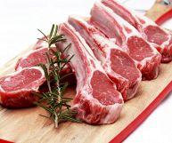 Su un tagliere, costolette di agnello crude, dalle carni invitanti; sopra è adagiato un rametto di rosmarino verde scuro; possono essere cucinate alla griglia
