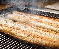 Due anguille tagliate a metà per il verso lungo; hanno carni sode, biancastre all'interno e rosolate in superficie; stanno terminando la cottura