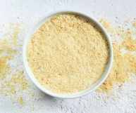 Pangrattato dal colore dorato in una scodella bianca e sul piano di lavoro su cui è appoggiata; ciotola e tavolo sono bianchi; vista dall’alto