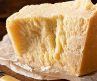 Fetta di Parmigiano Reggiano dal colore paglierino e dalla consistenza compatta; la crosta, più scura, presenta il tipico marchio DOP